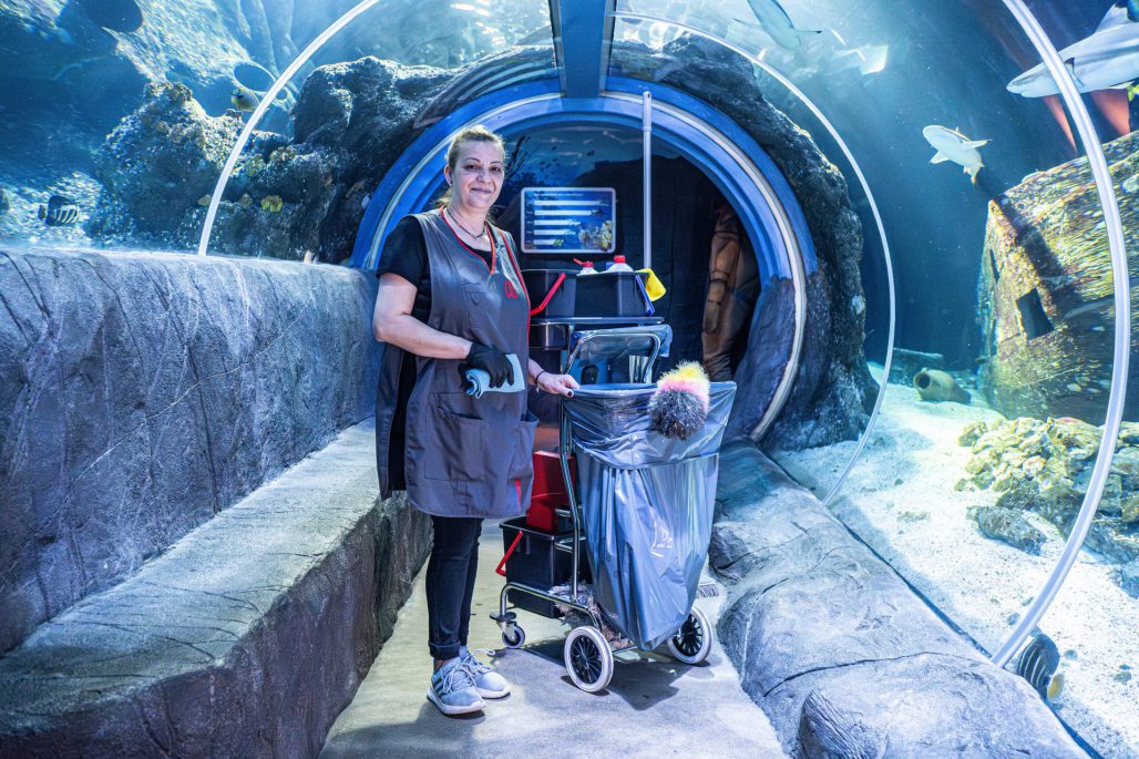 Sea Life Oberhausen: Reinigungskraft von Rudolf Weber Gebäudedienste vor dem großen Aquarium. Im Hintergrund schwimmen Haie.